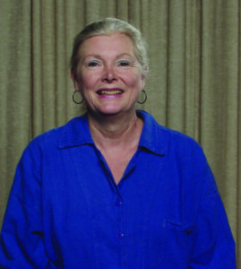 A woman wearing a blue shirt and posing for a portrait in front of a tan curtain.