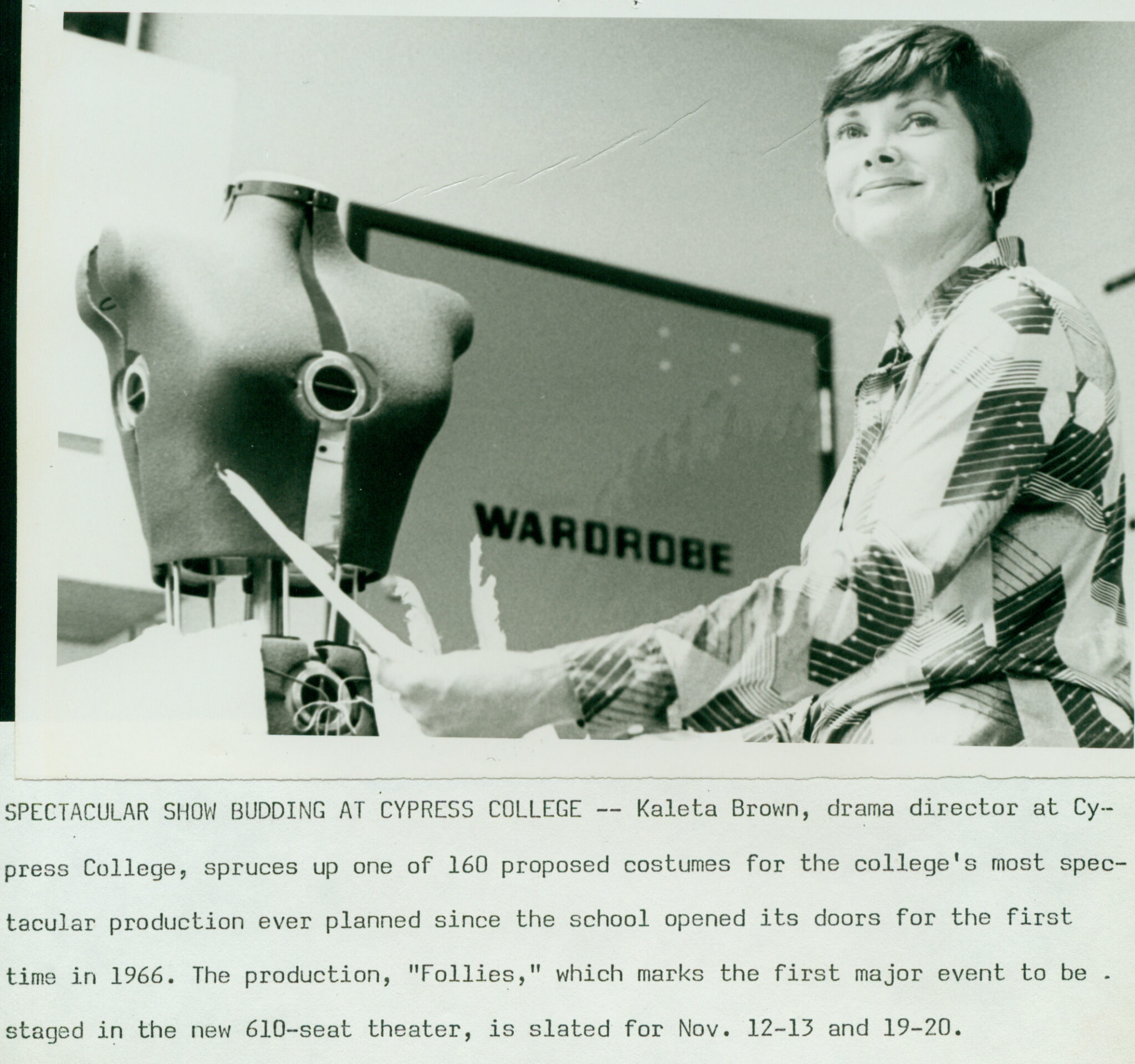 A woman stands in a theater costume shop in front of a partial mannequin. The text below the photo reads: " SPECTACULAR SHOW BUDDING AT CYPRESS COLLEGE -- Kaleta Brown, drama director at Cy.-press College, spruces up one of 160 proposed costumes for the college's most spec-tacular production ever planned since the school opened its doors for the first time in 1966. The production, "Follies," which marks the first major event to be staged in the new 610-seat theater, is slated for Nov. 12-13 and 19-20."