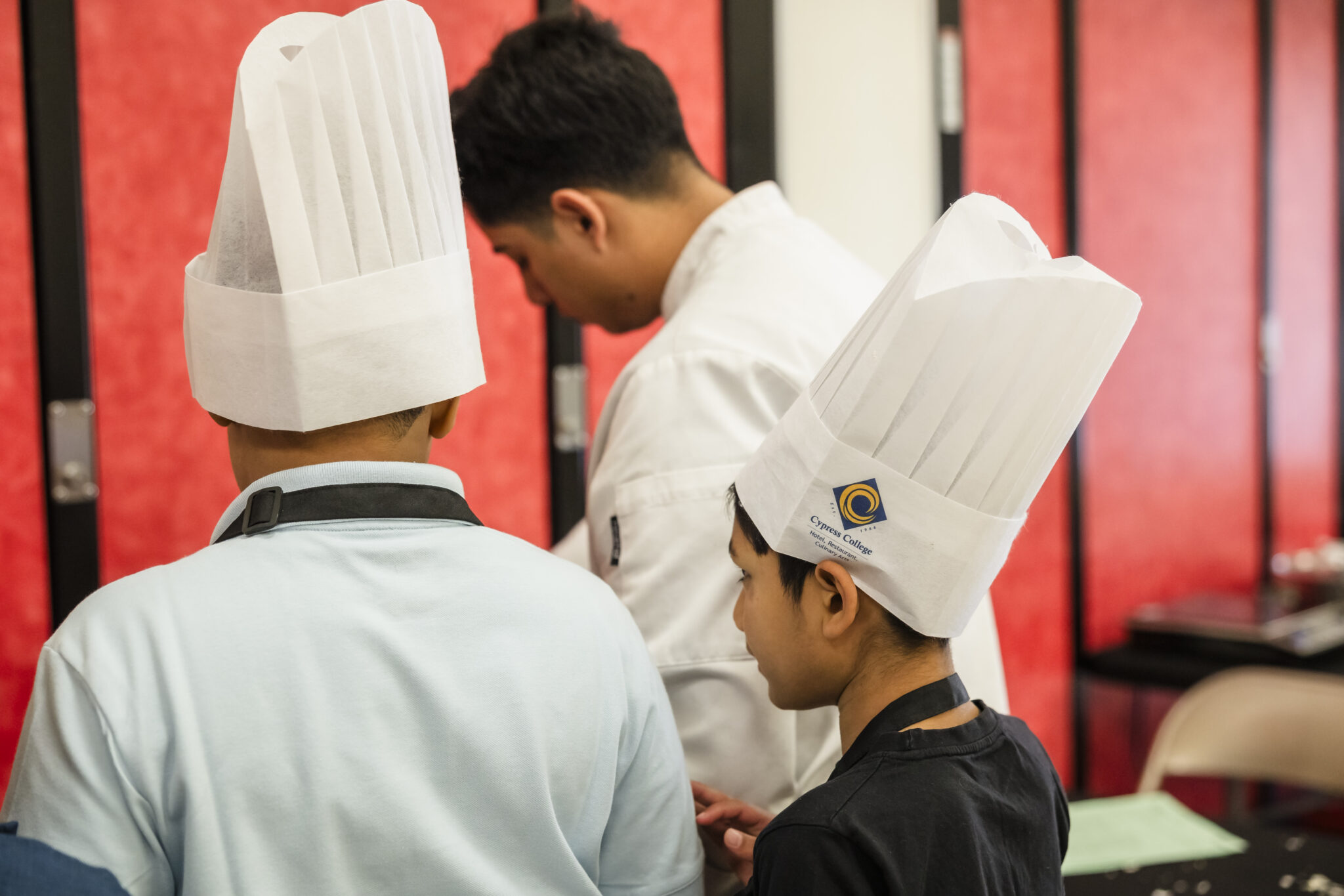 Elementary students look on as Cypress Students coach them in food preparation.