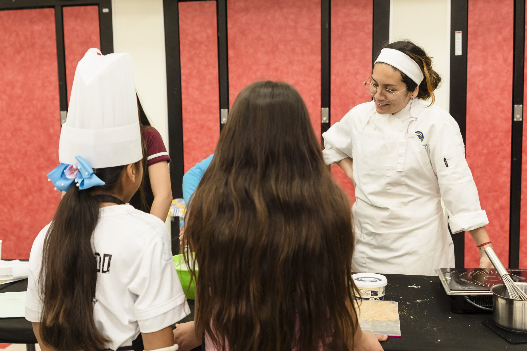 A Cypress College Culinary Arts student helps fourth and fifth graders with a main course dish. 