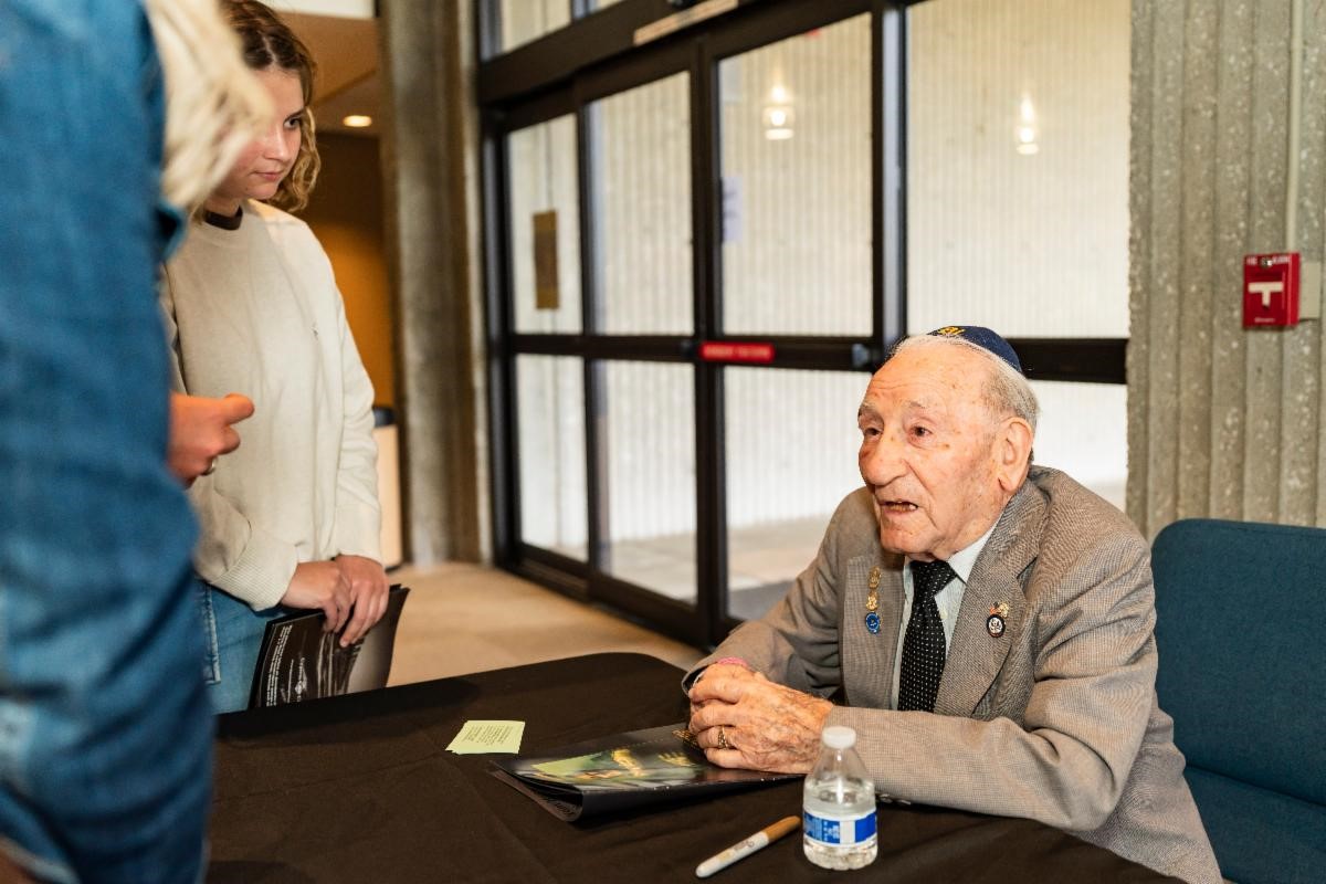 A survivor at his table speaking to a group of people at the pre-event signing.