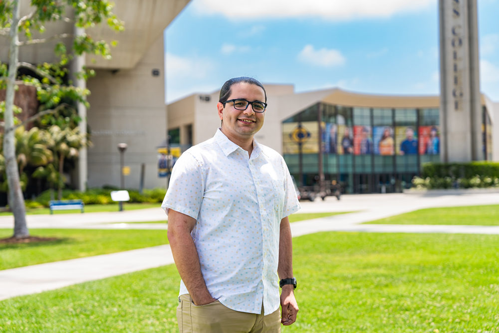 Alumnus Theodore Abdelmaseh stands in Gateway Plaza on a green lawn in front of the admissions and records building at Cypress College.